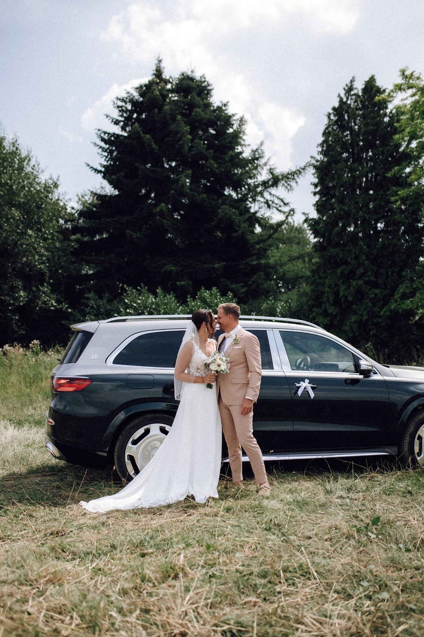 Braut und Bräutigam stehen vor dem Hochzeitsauto auf der Wiese