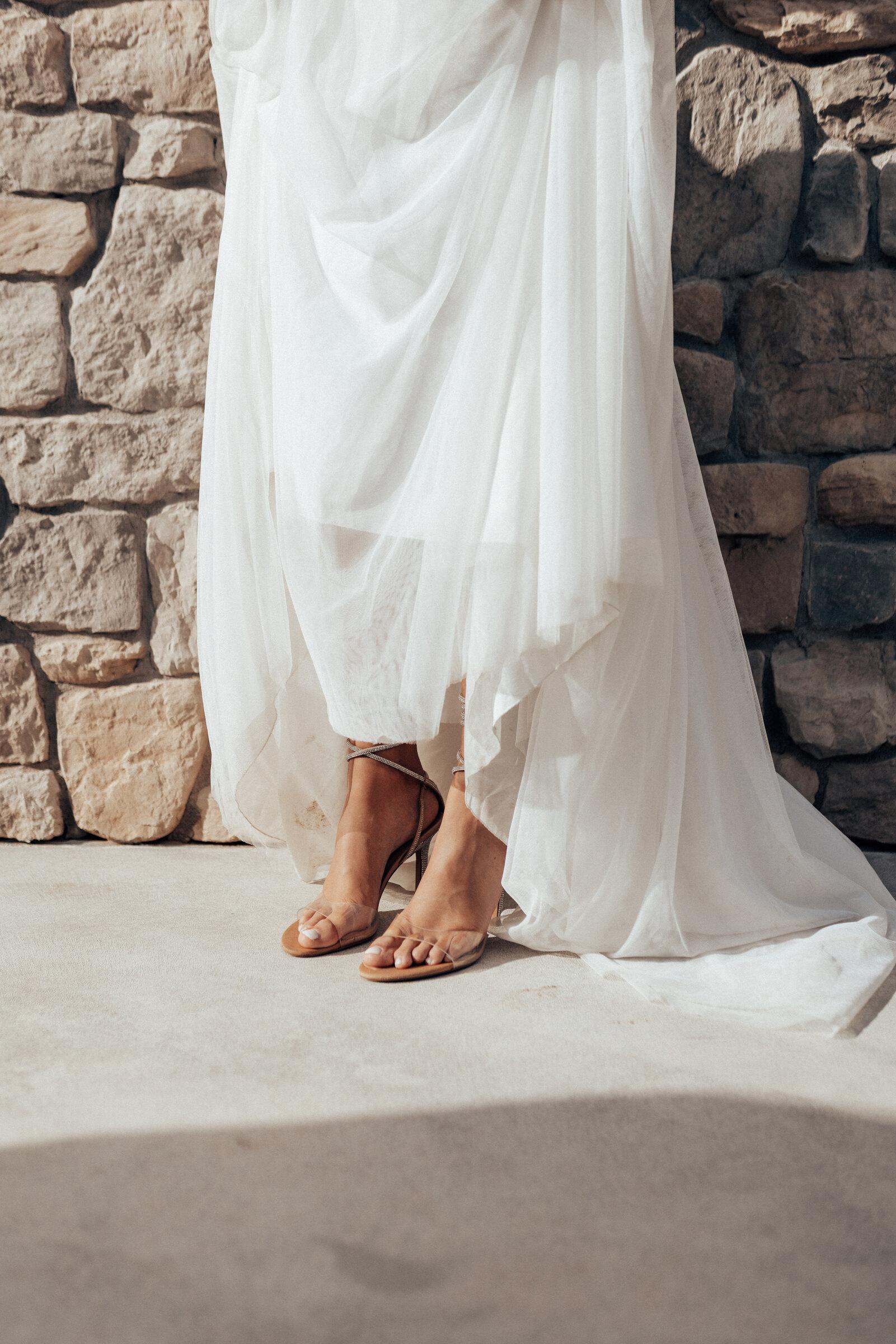 Detail: Brautkleid und Schuhe an einer Steinmauer