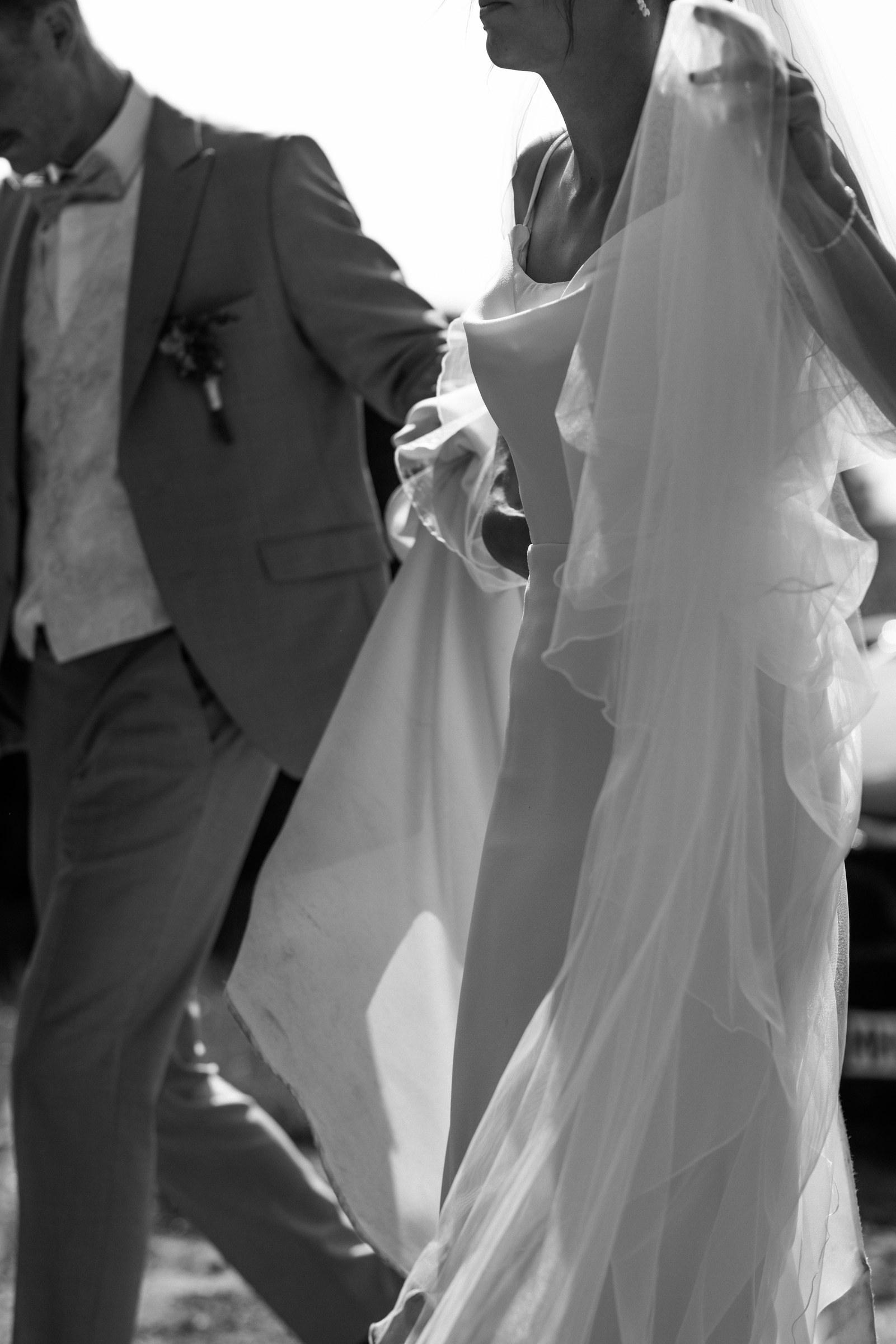 Celine und Philipp gehen Hand in Hand, ihr Schleier weht, Schwarzweiß