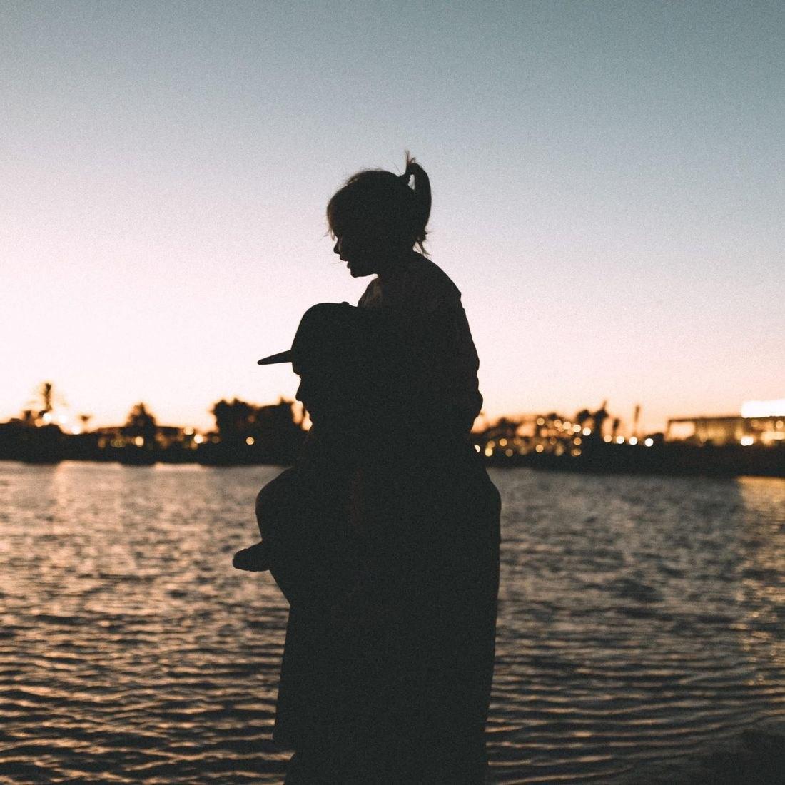 Silhouette von mir mit meiner Tochter auf den Schultern am Wasser